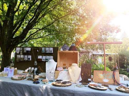 A display of handmade jewelry on a table under a tree, with sunlight filtering through the leaves.