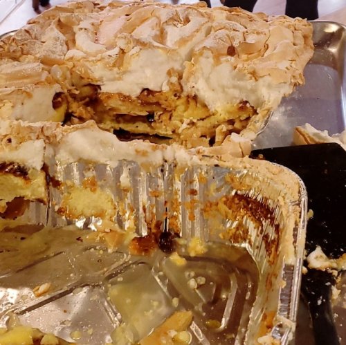 A partially eaten pie with a meringue topping, revealing layers of filling and crust in a metal tray.