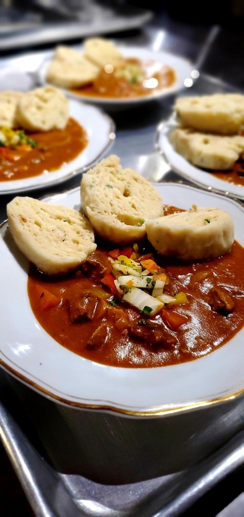 A bowl of rich stew with chunks of meat, garnished with vegetables, served with fluffy dumplings on the side.