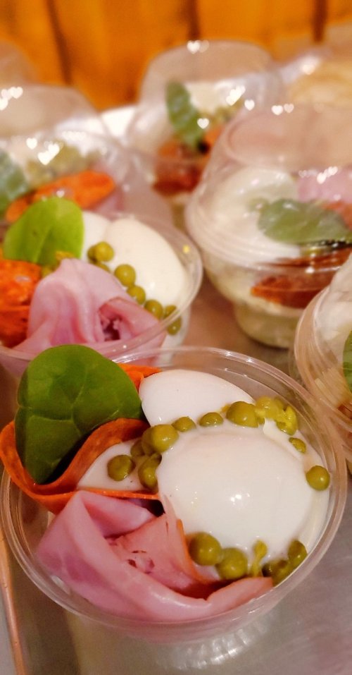 Assorted appetizers in clear cups, featuring ham, peas, and fresh greens.