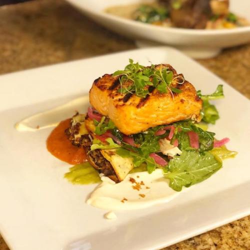 A beautifully plated dish featuring grilled salmon atop a bed of greens, with sauces and garnishes.