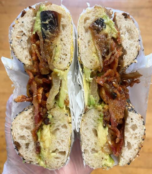 A cross-section of a sandwich filled with crispy bacon, avocado, and caramelized onions on a sesame seed bun.