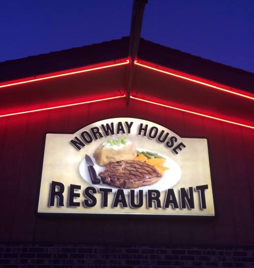 Sign for Norway House Restaurant featuring a steak dinner, illuminated with red neon lights at dusk.