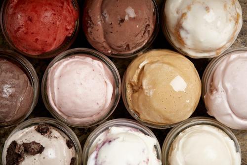 A variety of ice cream scoops in glass jars, featuring flavors like chocolate, strawberry, and vanilla.