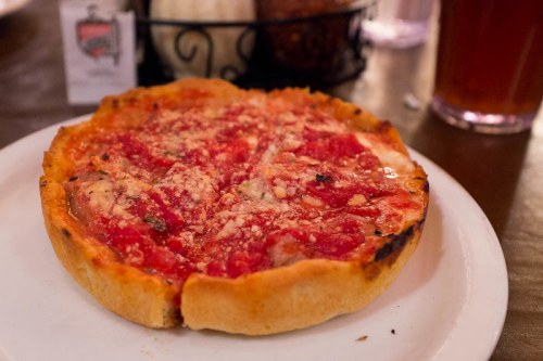 A deep-dish pizza topped with tomato sauce and cheese, served on a white plate.