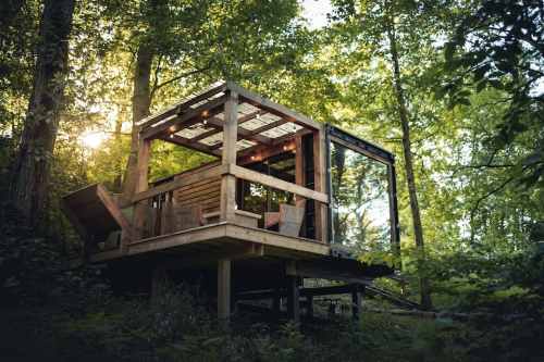 A modern treehouse nestled among lush green trees, featuring a wooden deck and large windows.