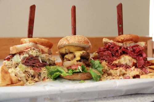 Three stacked burgers with toppings, including lettuce and cheese, served with crispy potato chips on a white paper.