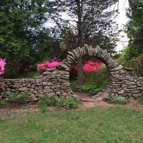 A stone archway surrounded by lush greenery and vibrant pink flowers in a serene garden setting.
