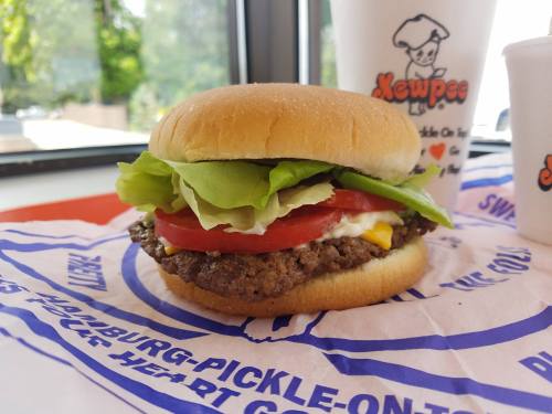 A close-up of a hamburger with lettuce, tomato, and mustard on a bun, placed on a colorful paper wrapper.