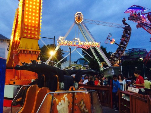 A vibrant amusement park scene featuring the Sea Dragon ride, with colorful lights and a crowd of excited visitors.
