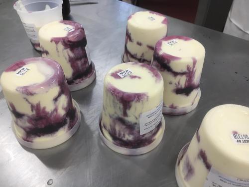 Six containers of marbled yogurt or dessert with a purple swirl, placed on a stainless steel surface.