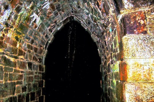 A dark stone archway with a textured, weathered surface, leading into an unknown space.