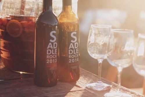 Two wine bottles labeled "Saddle Rock 2013" and "Saddle Rock 2014" beside empty wine glasses and a pitcher.