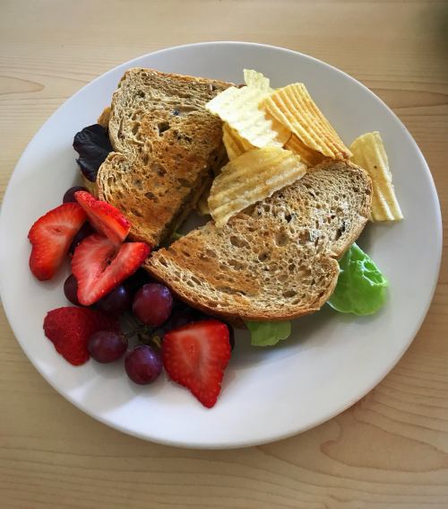 A plate with a sandwich, potato chips, strawberries, and grapes arranged on a wooden table.