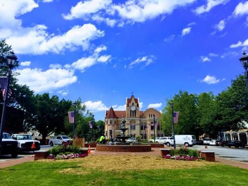 A sunny town square with a clock tower, surrounded by greenery, flowers, and American flags.