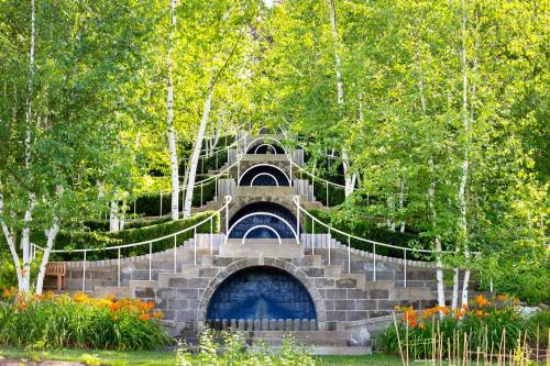 A serene landscape featuring a cascading stone fountain surrounded by lush greenery and vibrant orange flowers.