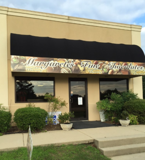 Exterior of a chocolate shop named "Margaret's Fine Chocolates," featuring a sign and a welcoming entrance.
