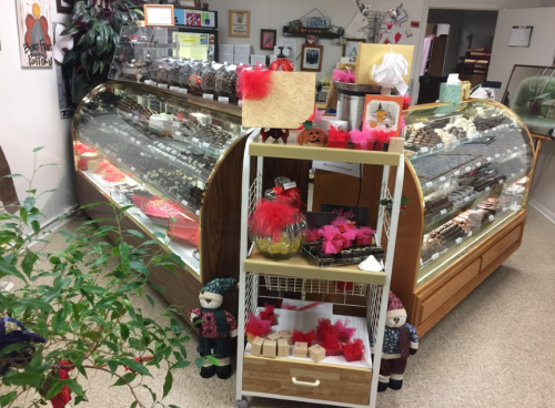 A cozy candy shop interior featuring glass display cases filled with sweets and a festive gift display in the center.