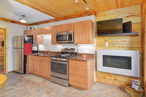 Cozy kitchen with wooden accents, stainless steel appliances, and a modern gas stove. Features a wall-mounted TV and fireplace.