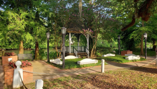 A serene park scene featuring a gazebo surrounded by lush greenery and decorative lamps.