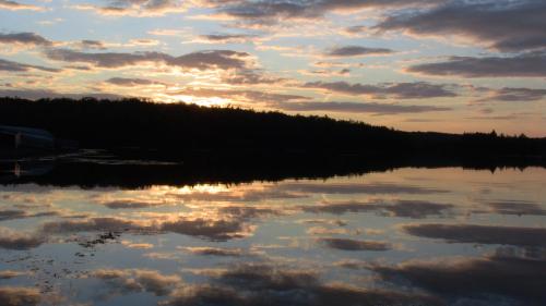 A serene sunset over a calm lake, with clouds reflecting on the water's surface and a silhouette of trees in the background.