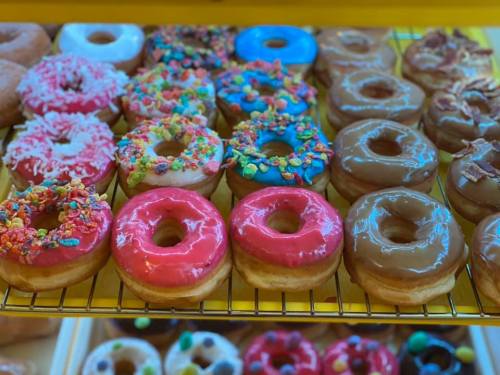 A colorful assortment of donuts with various toppings, including sprinkles, frosting, and bacon, displayed on a rack.
