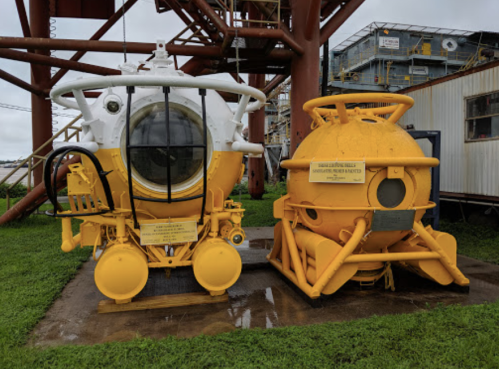 Two yellow submarines displayed outdoors, one with a large viewing window, next to a smaller, spherical submersible.
