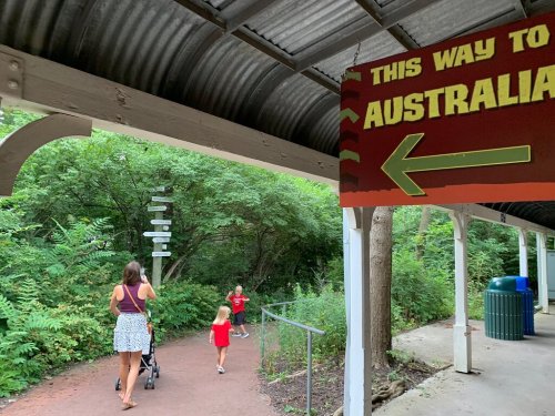 A sign pointing left to "Australia" with a path leading into greenery, where two children and an adult walk.
