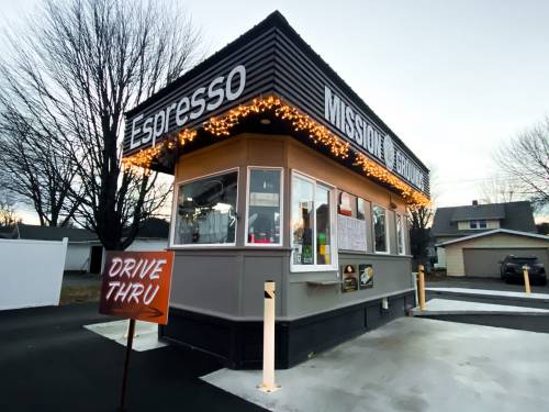 A drive-thru coffee stand with festive lights, featuring a menu board and a sign pointing to the drive-thru entrance.