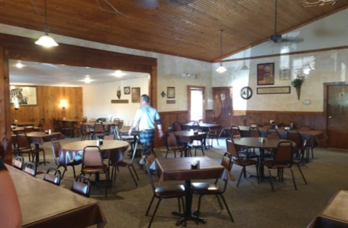 A spacious, rustic dining area with wooden tables and chairs, featuring warm lighting and a cozy atmosphere.