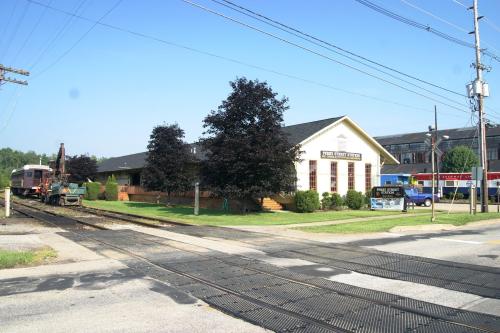 A train station building with trees nearby, located at a railroad crossing on a clear day.