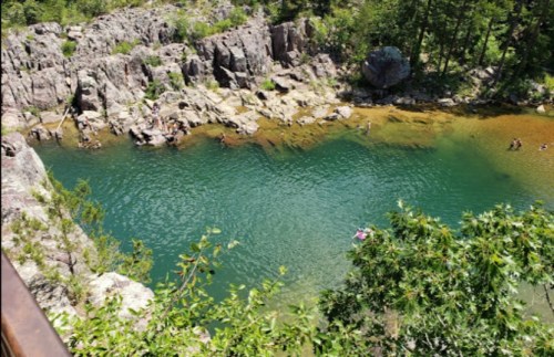A serene natural pool surrounded by rocky cliffs and lush greenery, with people enjoying the water.