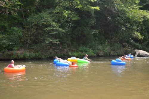 A group of people floating on colorful inner tubes in a calm river surrounded by lush greenery.