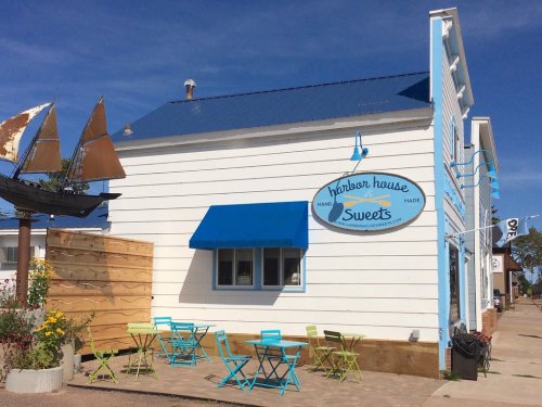 A charming white building with a blue roof and sign reading "Harbor House Sweets," featuring outdoor seating.