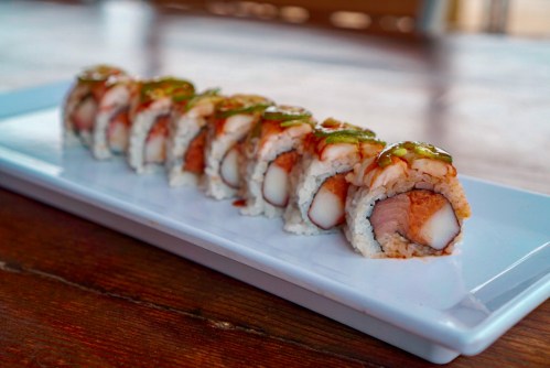 A plate of sushi rolls with various fillings, drizzled with sauce, on a wooden table.