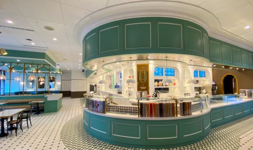 A stylish café interior featuring a curved counter, display cases, and elegant lighting in a green and white color scheme.