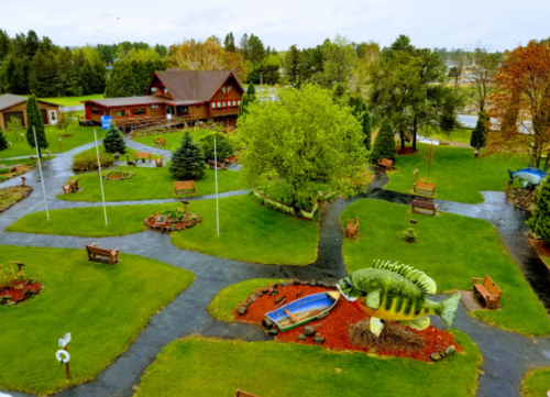 Aerial view of a park with green lawns, trees, benches, and a large fish sculpture in the center.