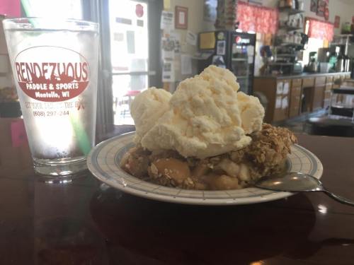 A plate of warm dessert topped with ice cream, next to a glass of water in a cozy café setting.