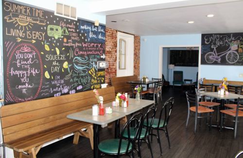 A cozy café interior with wooden benches, tables, and colorful chalkboard art on the walls. Bright and inviting atmosphere.