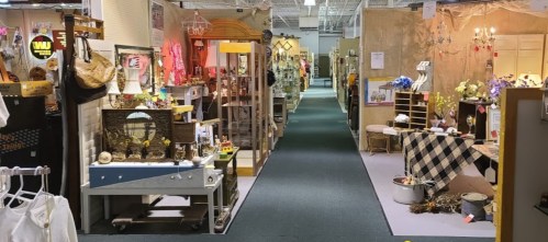 A spacious vintage market with various booths displaying antiques, decor, and crafts along a central walkway.