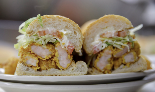Close-up of a sandwich with fried chicken, lettuce, tomato, and mayonnaise on a soft bun, cut in half.