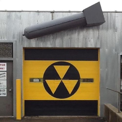 A garage door with a yellow and black radiation symbol and a large gray object resembling a missile above it.