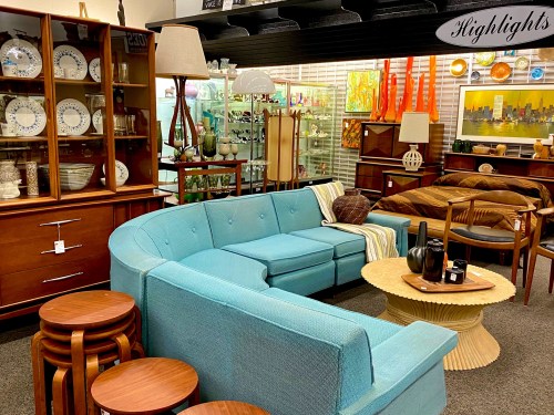 A stylish vintage furniture display featuring a turquoise sectional sofa, wooden tables, and decorative items.
