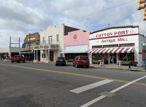 A street view featuring vintage storefronts, including Rialto and Cotton Port Antique Mall, with parked cars and cloudy skies.