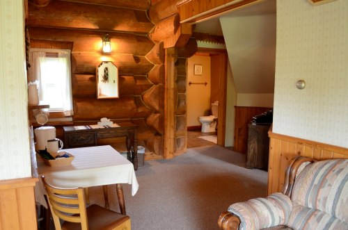 Cozy log cabin interior featuring a dining table, seating area, and a view of a bathroom door. Warm, rustic decor.