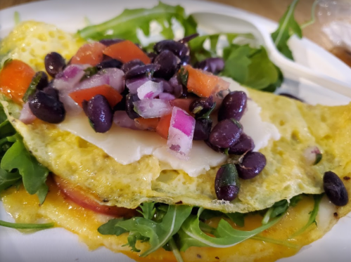 A colorful omelette topped with black beans, diced tomatoes, onions, and served on a bed of fresh greens.