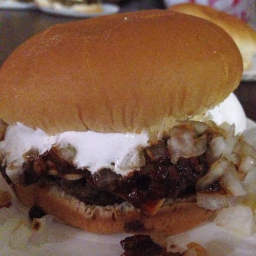 A close-up of a hamburger with a soft bun, filled with chopped onions and a dark, savory meat patty.