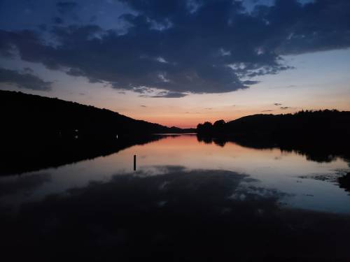 A serene river at dusk, reflecting colorful clouds and silhouettes of trees against a twilight sky.
