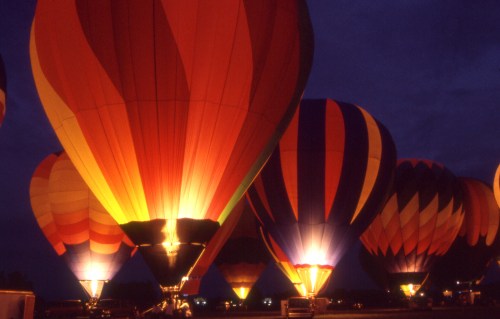 Colorful hot air balloons illuminated at night, creating a vibrant display against a dark sky.