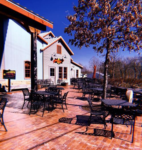 Outdoor seating area with black metal tables and chairs, surrounded by trees and a blue sky.